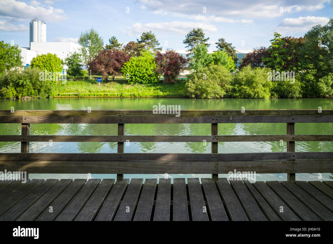 Un ponton en bois avec rampes en bois en face d'une rivière avec des arbres et de la végétation sous un ciel bleu avec des nuages blancs. Banque D'Images