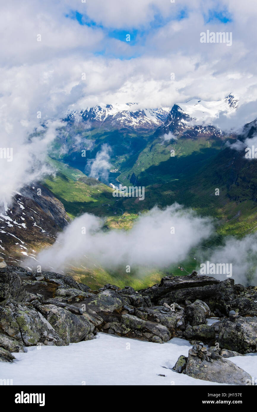 Vue vers le bas à travers les nuages de Geirangerfjorden avec montagnes aux sommets enneigés de la montagne Dalsnibba en été. Sunnmore, Geiranger, Norvège région Banque D'Images