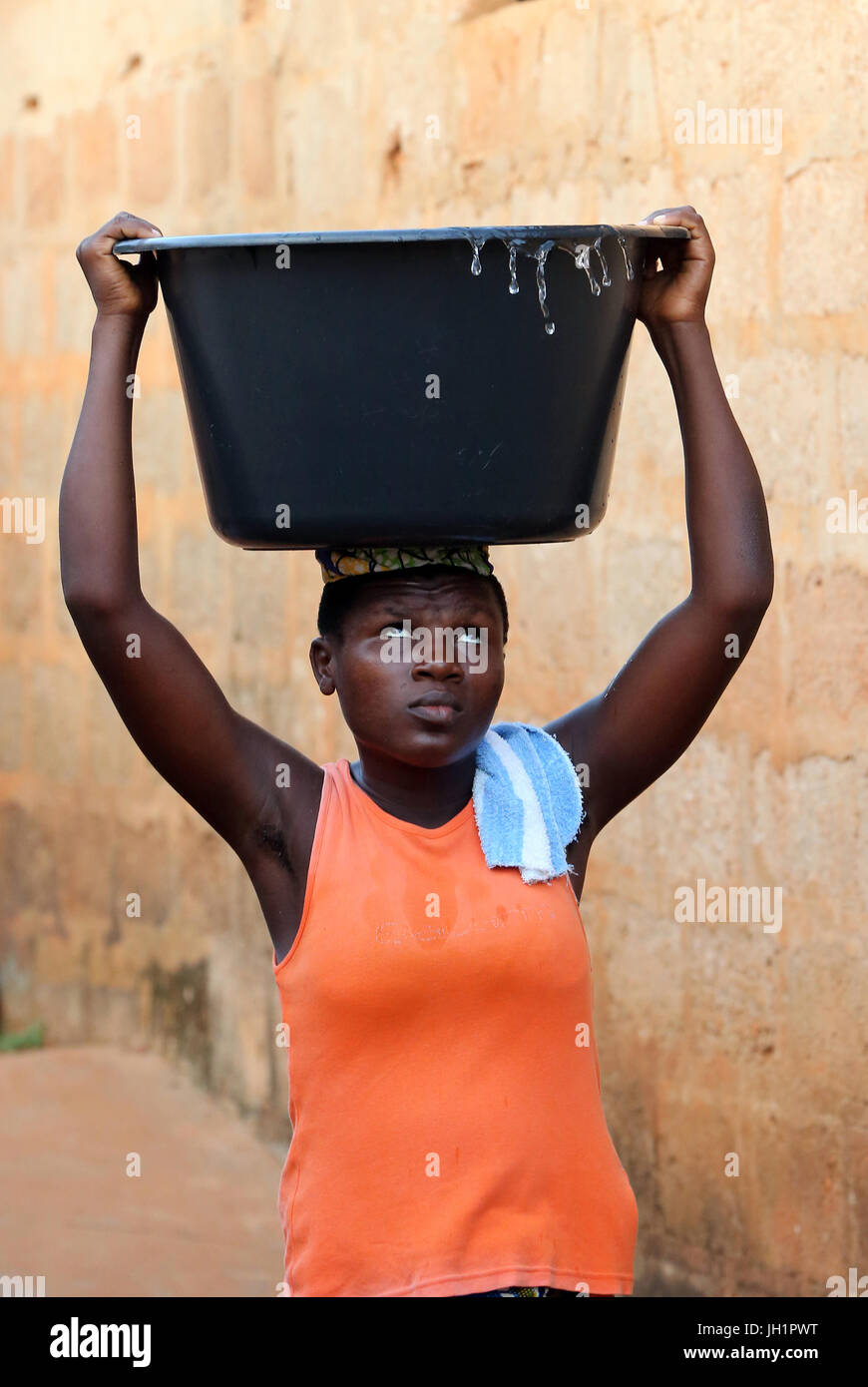 La vie du village africain. Corvée d'eau. Petite fille africaine portant un bassin d'eau sur la tête. Togoville. Le Togo. Banque D'Images