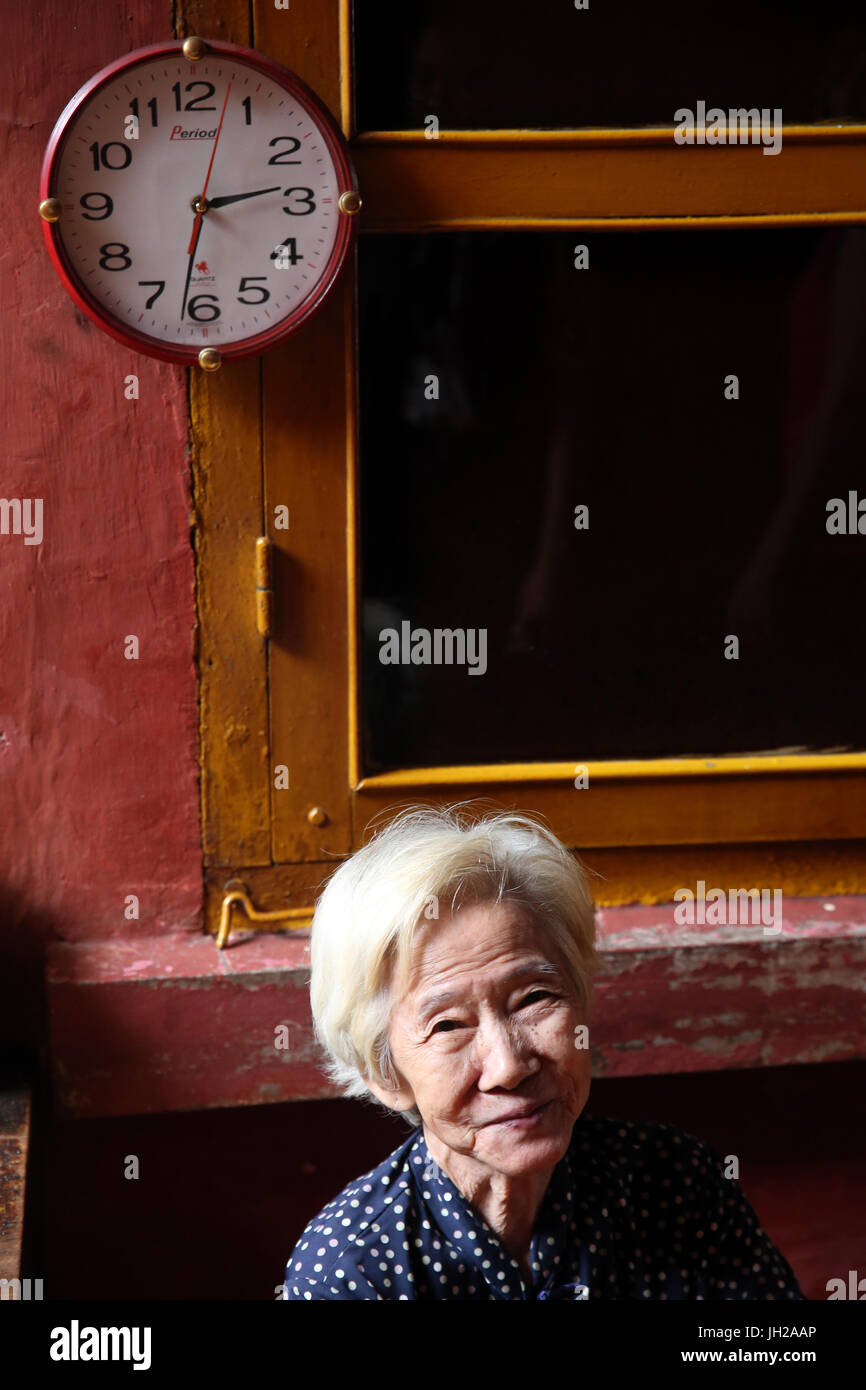 Réveil sur le mur et le vieille femme. Ho Chi Minh Ville. Le Vietnam. Banque D'Images