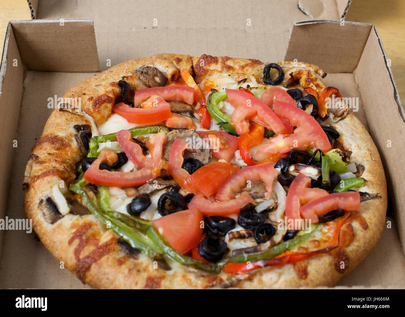 Gros plan sur pizza végétarienne en boîte carton servi avec tomates, olives noires, champignons, oignons, poivrons et mozzarella Banque D'Images