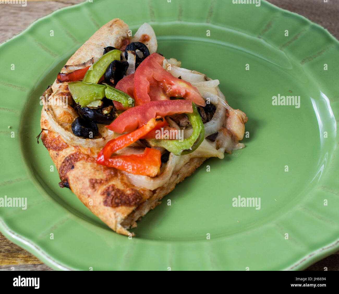 Gros plan sur pizza végétarienne avec tomates, olives noires, champignons, oignons, poivrons et mozzarella, sur plaque verte, contre fond de bois Banque D'Images