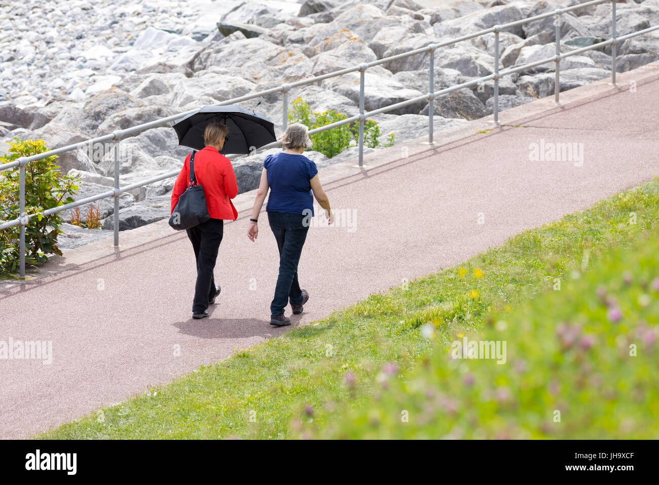 Deux femme marchant dans le chemin du littoral du pays de Galles à Rhos-on-Sea à côté de Colwyn Bay dans le Nord du Pays de Galles sur une journée chaude en été avec un seul tenant un parapluie pour l'ombre Banque D'Images