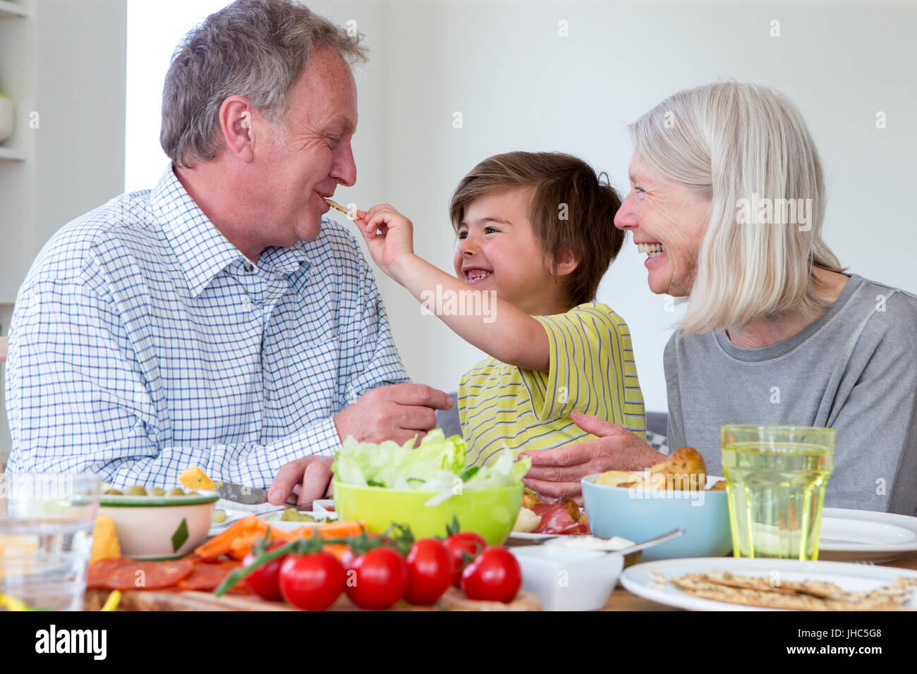 Petit garçon est l'alimentation de son grand-père un craquelin crème tout en ayant un style méditerranéen déjeuner avec les deux grands-parents. Banque D'Images