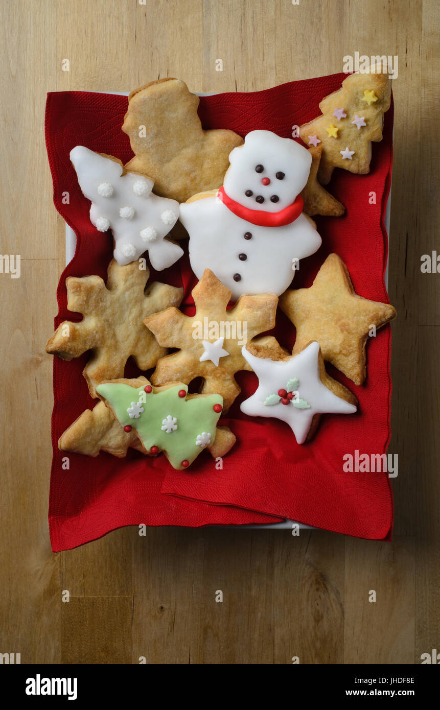 Coup de frais généraux d'une variété de plaine et iced (dépoli) des biscuits de Noël (cookies) dans un récipient blanc rectangulaire avec serviettes en bois rouge sur Banque D'Images