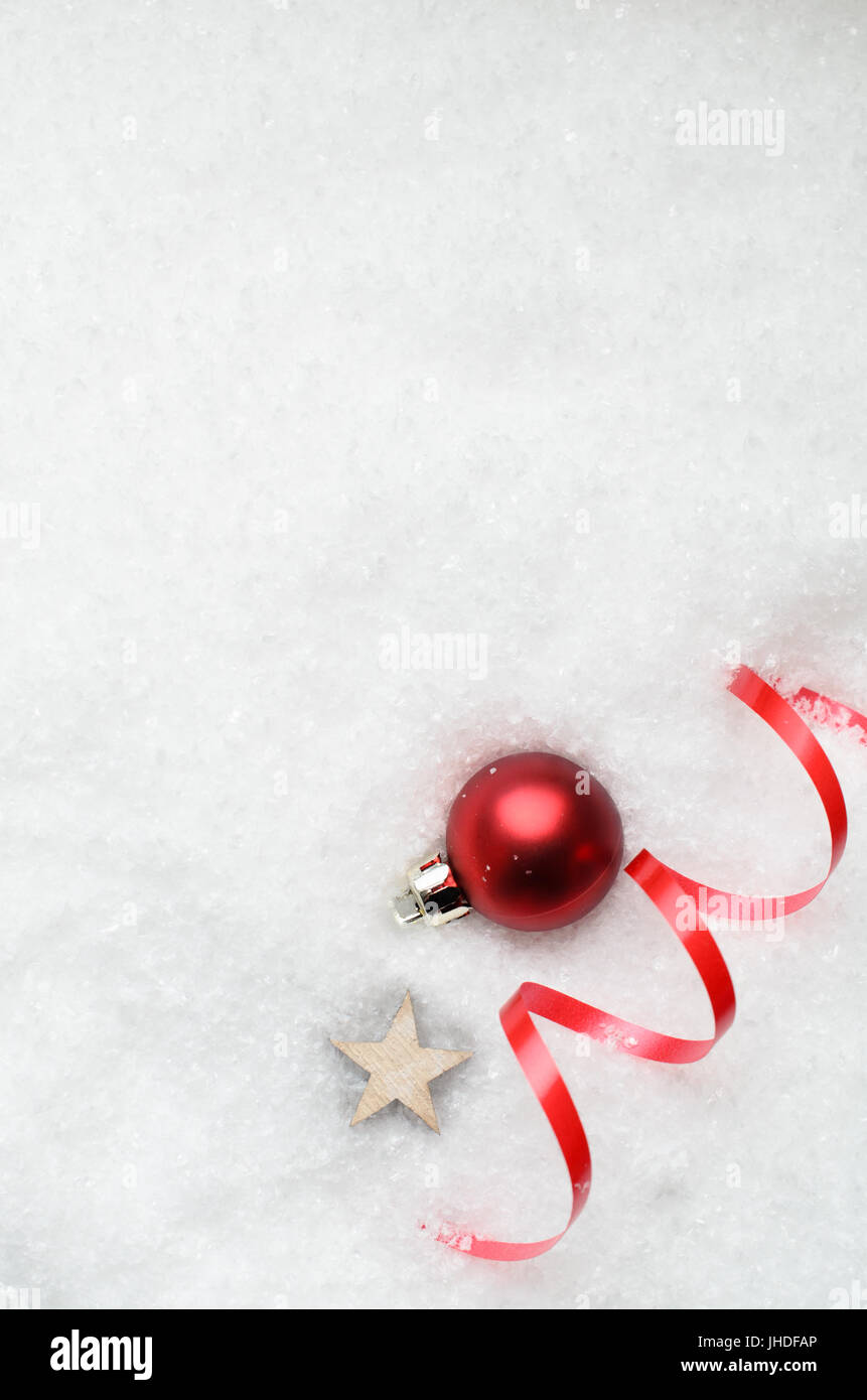 Frais généraux de fond de Noël avec ruban décoratif babiole rouge, étoile en bois swirl et partiellement dans le blanc de la neige artificielle sur le coin inférieur droit Banque D'Images