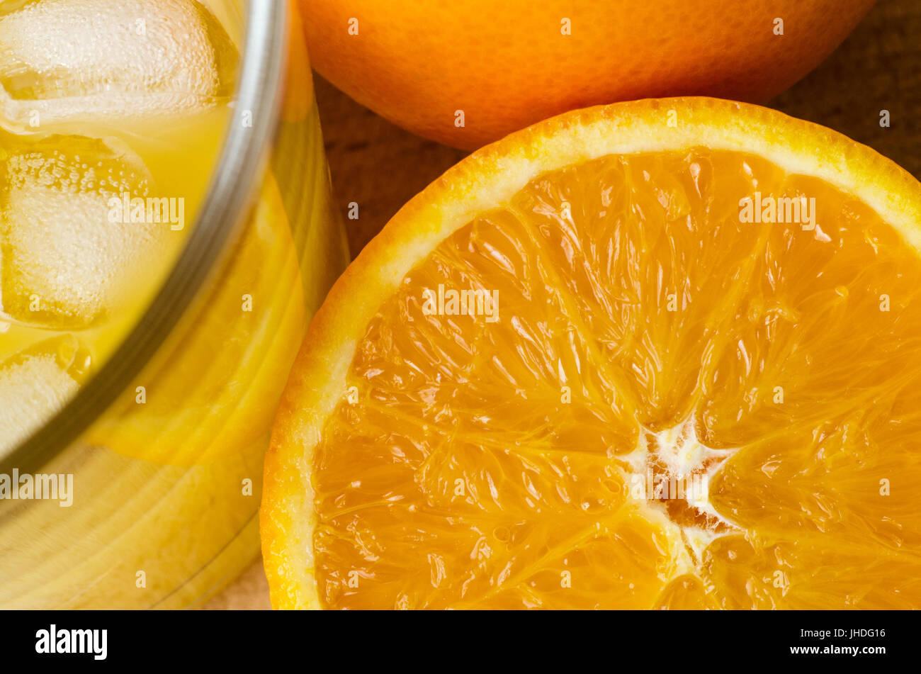 Frais généraux en angle close up shot de jus d'orange frais dans le verre avec des glaçons. une demi-orange avec pulpe et exposés ensemble orange non pelée sur ta en bois Banque D'Images