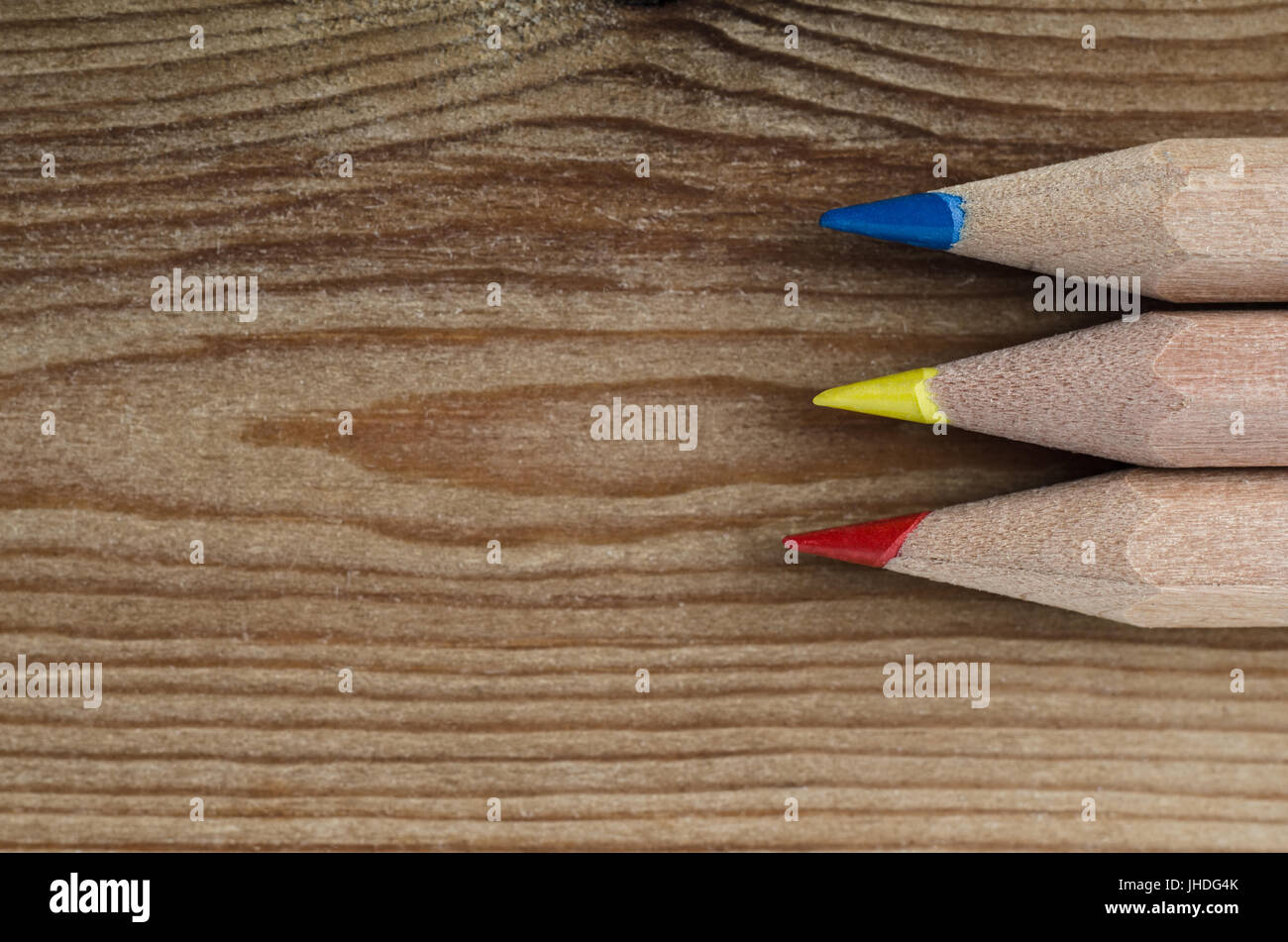 Trois crayons représentant les couleurs primaires rouge, jaune et bleu avec des conseils pointant vers la gauche en l'espace de copie sur du bois clair. Banque D'Images