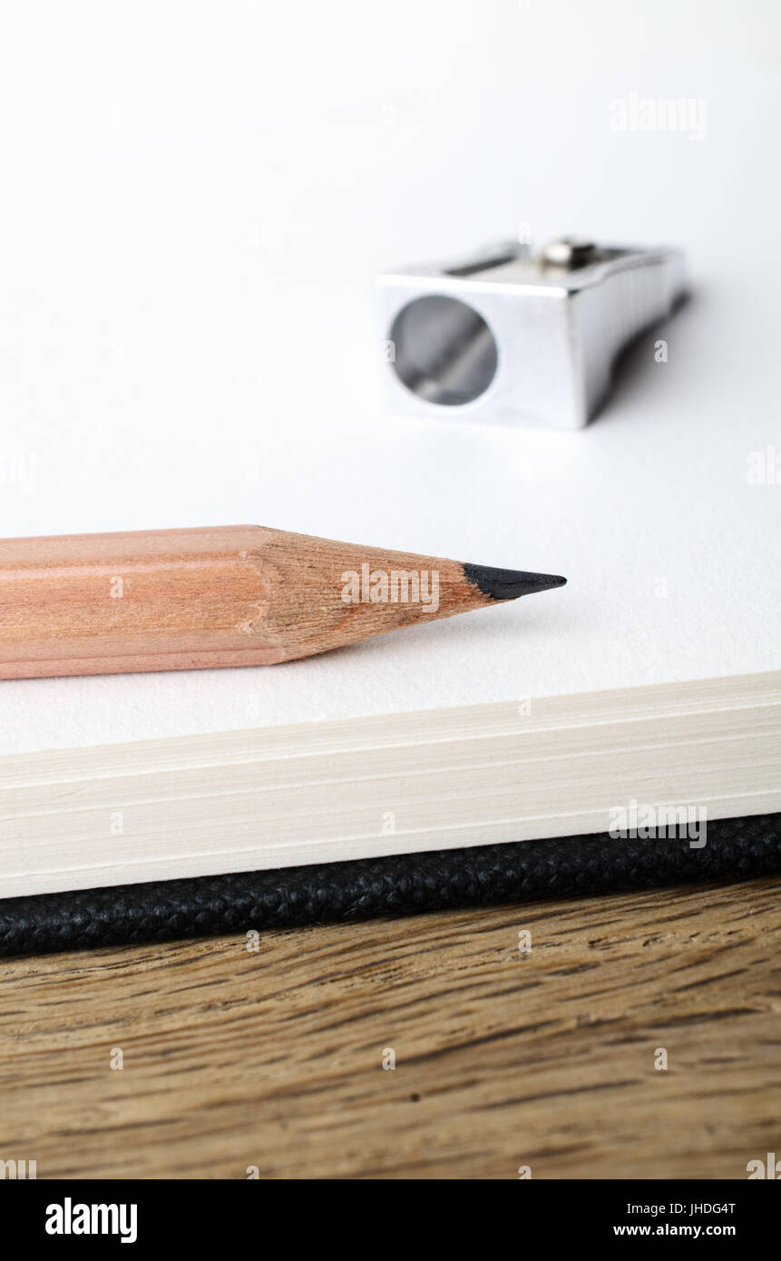 L'angle de près de l'extrémité d'un crayon dessin au graphite en bois au bord d'un carnet de croquis vierge page avec sharpener in soft focus arrière-plan. Banque D'Images