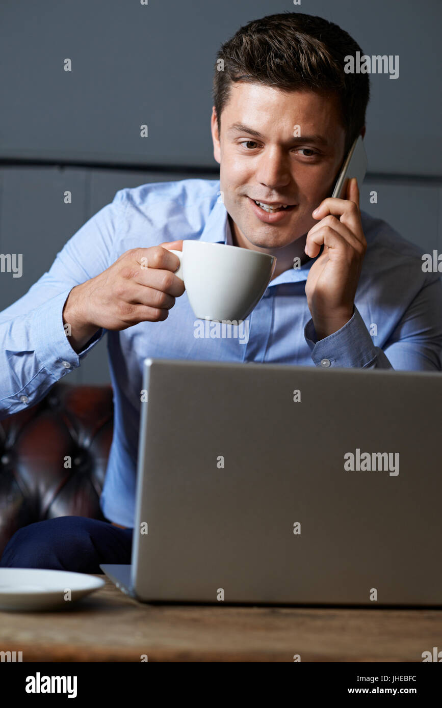 Businessman Talking On Mobile Phone Working On Laptop In Internet Cafe Banque D'Images