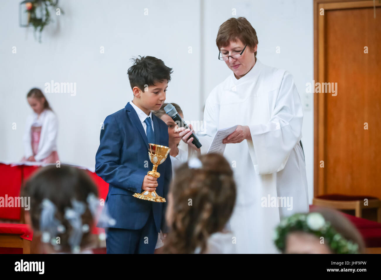 NANDLSTADT, ALLEMAGNE - Mai 7, 2017 : un jeune garçon communion lecture des versets de l'étude tenue par les prêtres assistant à la première communion dans Nandls Banque D'Images