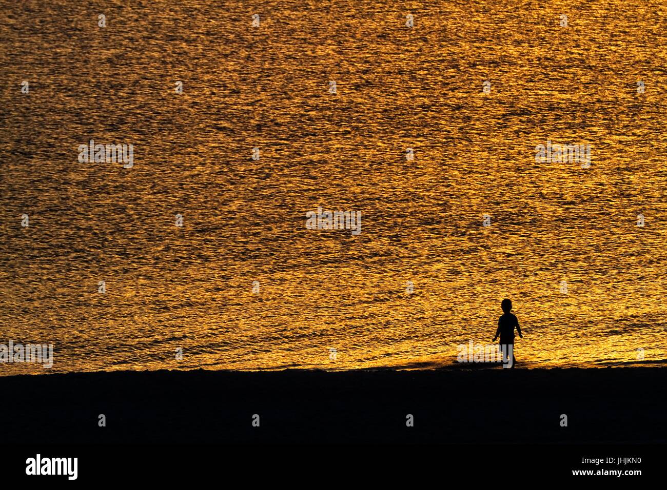 Coucher du soleil doré. Bord de mer. Silhouettes d'enfants. Banque D'Images