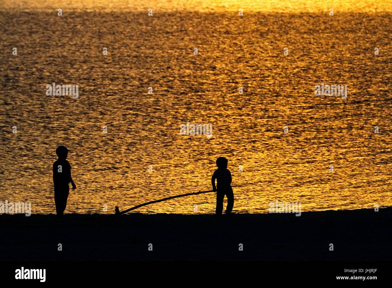Coucher du soleil doré. Bord de mer. Silhouettes d'enfants. Banque D'Images