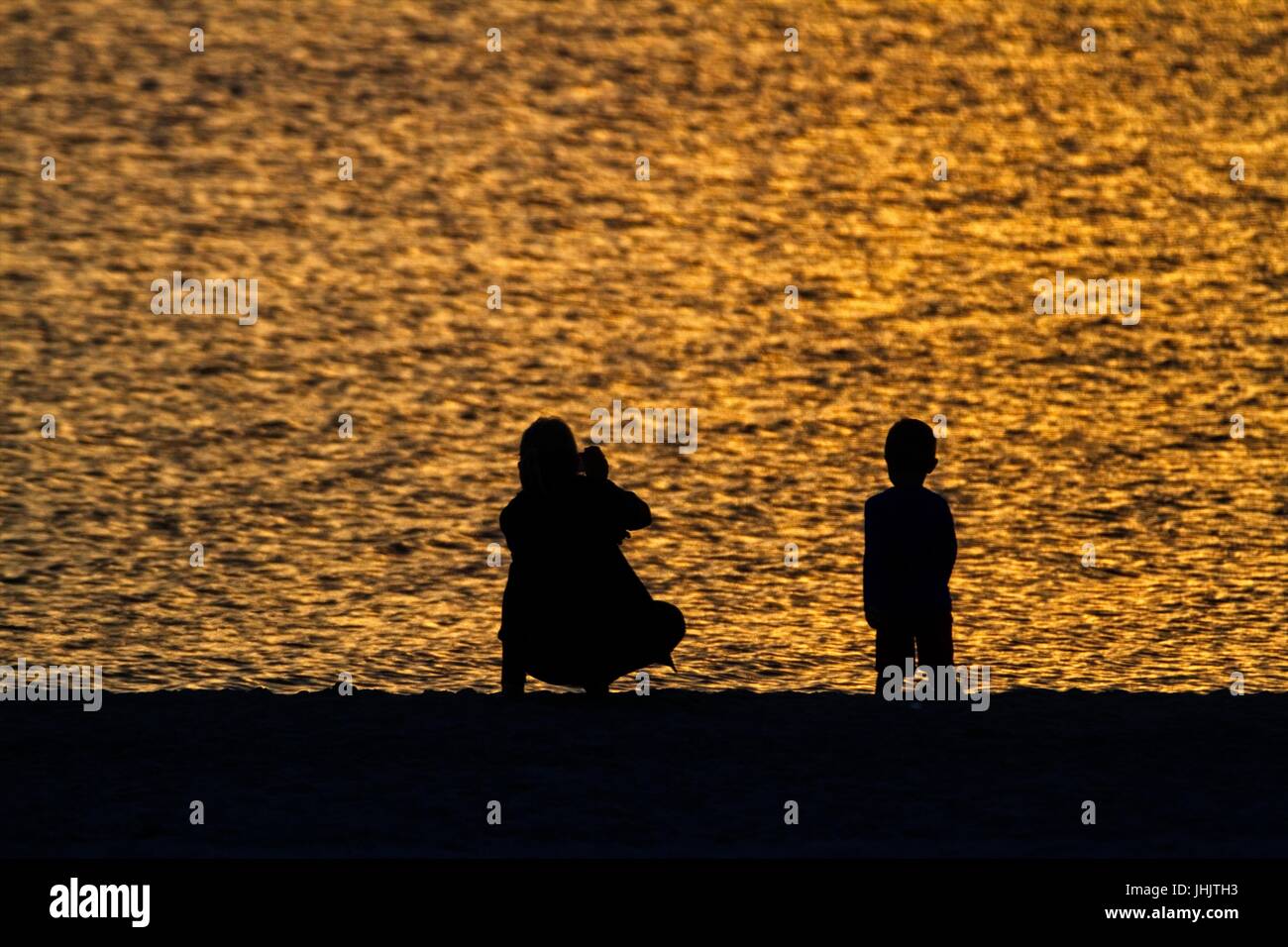 Coucher du soleil doré. Bord de mer. Silhouettes de la mère et l'enfant. Banque D'Images