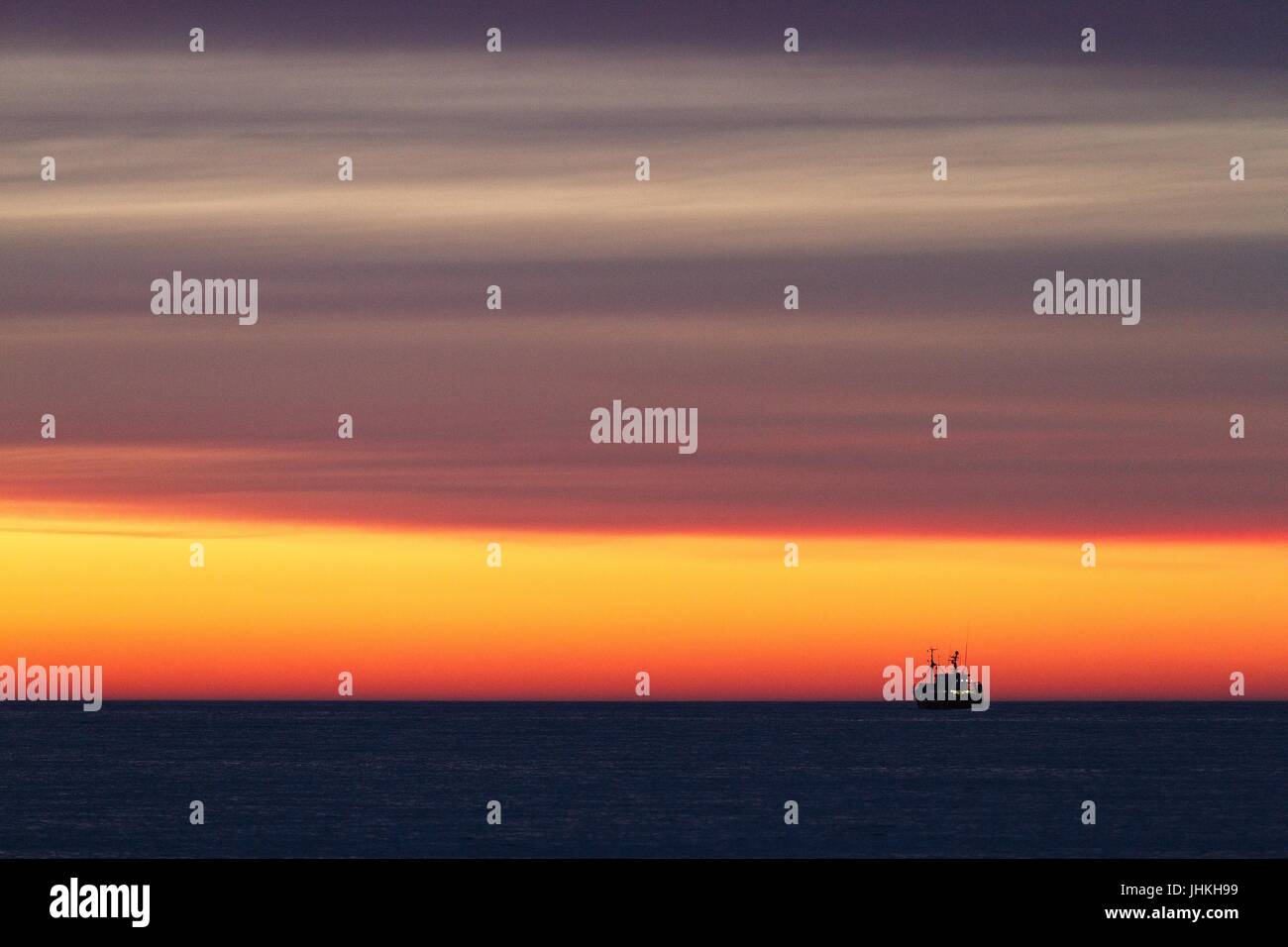 Silhouette d'un bateau de pêche sur la mer juste après le coucher du soleil. Couleur rouge jaune doré. Ciel avec nuages. Quelques lumières sur le bateau de pêche. Banque D'Images