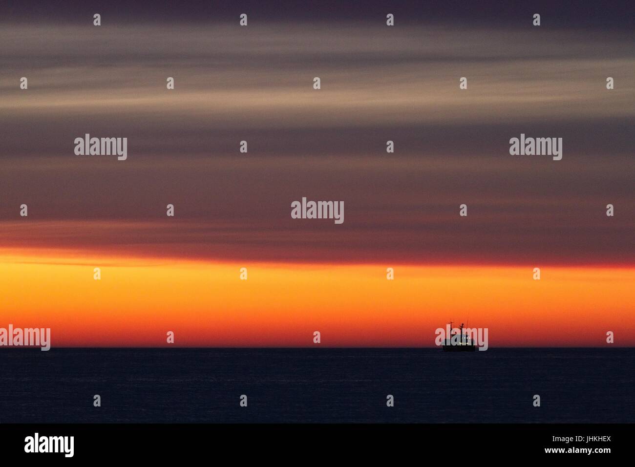 Silhouette d'un bateau de pêche sur la mer juste après le coucher du soleil. Couleur rouge jaune doré. Ciel avec nuages. Quelques lumières sur le bateau de pêche. Banque D'Images