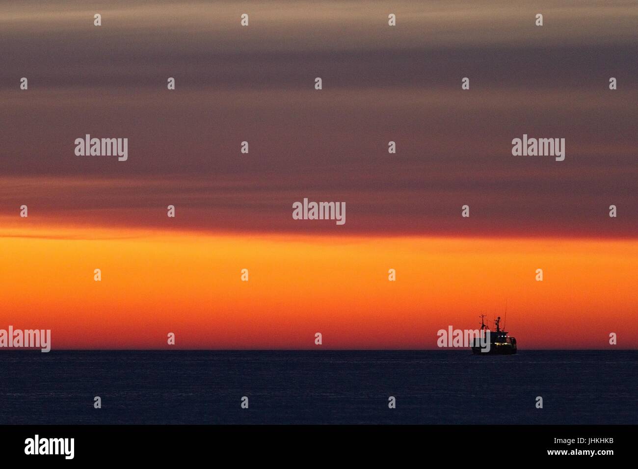 Silhouette d'un bateau de pêche sur la mer juste après le coucher du soleil. Couleur rouge jaune doré. Ciel avec nuages. Quelques lumières sur le bateau de pêche. Banque D'Images