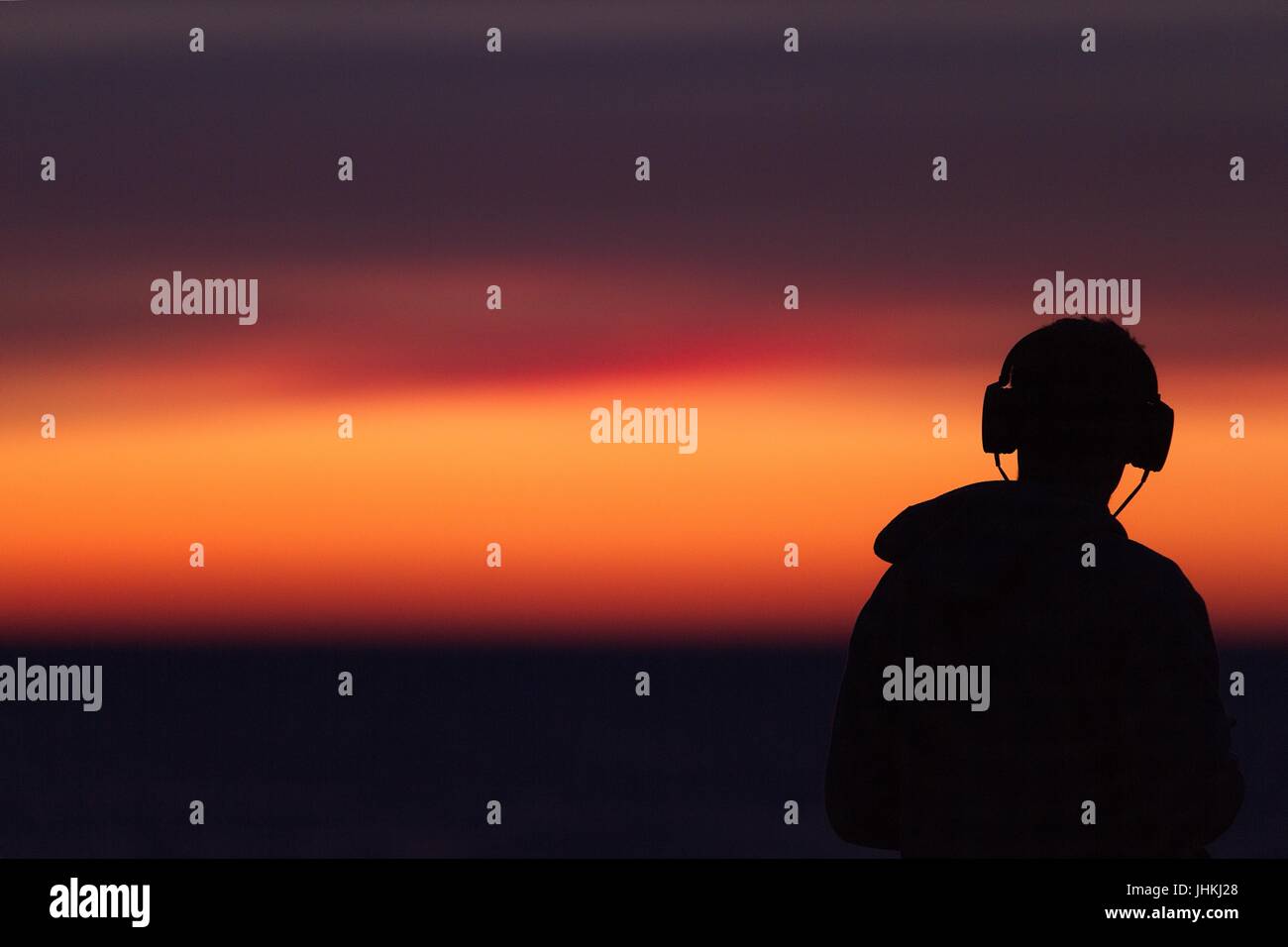 Silhouette de l'homme dans le casque / casque / écouteurs pendant le coucher du soleil au bord de la mer Banque D'Images