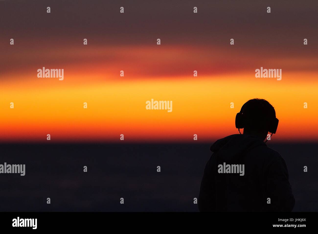 Silhouette de l'homme dans le casque / casque / écouteurs pendant le coucher du soleil au bord de la mer Banque D'Images