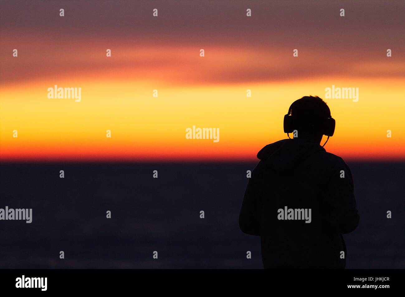 Silhouette de l'homme dans le casque / casque / écouteurs pendant le coucher du soleil au bord de la mer Banque D'Images