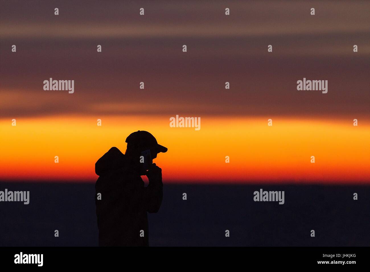 Silhouette de l'homme avec le mobile/portable pendant le coucher du soleil au bord de la mer. L'homme à une casquette de baseball. Banque D'Images