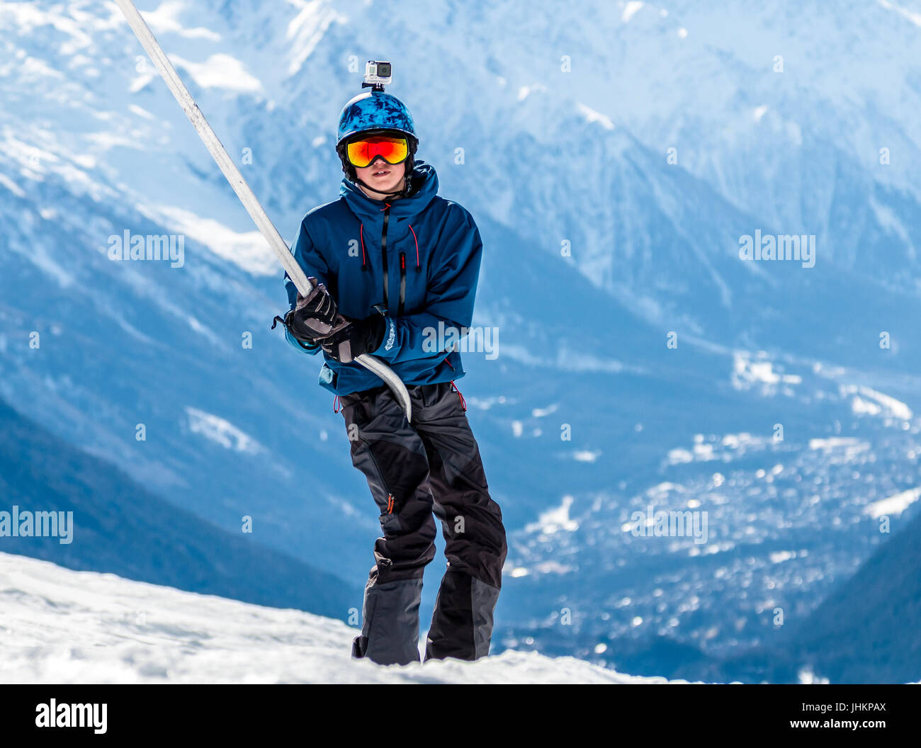 Snowboarder dans rainbow lunettes et casque bleu à l'aide d'un ascenseur de ski - snowboard un glisser-déplacer ou un type poma dans la vallée de Chamonix dans l'arrière-plan Banque D'Images