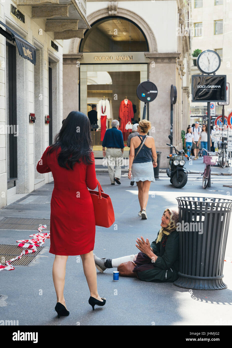 Femme portant un sac de transport de luxe en passant par un mendiant, dans le luxueux centre de Milan Italie Banque D'Images