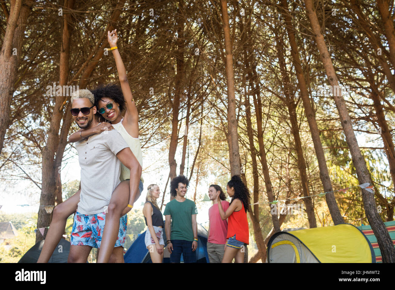 Portrait of happy man piggybacking woman avec des amis en arrière-plan de camping Banque D'Images