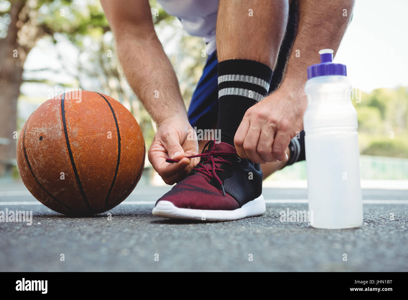 Joueur de basket-ball de la section basse lacet attachant alors que crouching en cour Banque D'Images