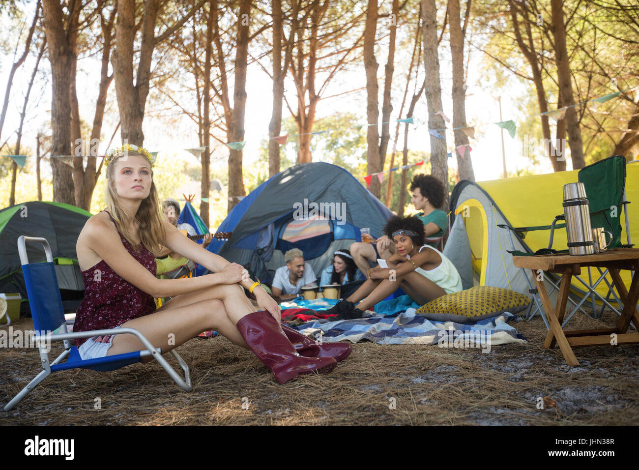 Thoughtful woman sitting on chair avec des amis en arrière-plan de camping Banque D'Images