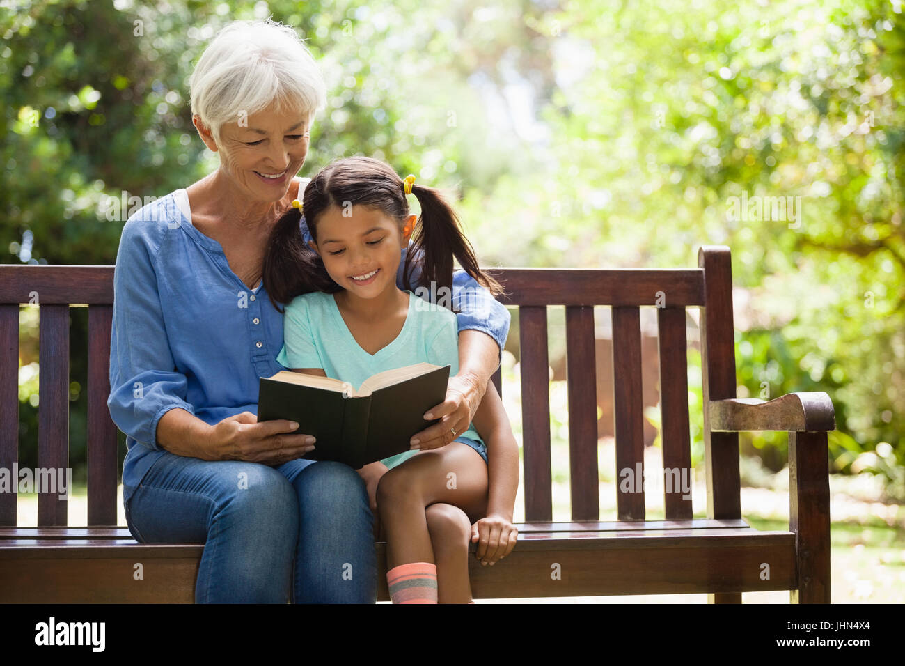 Father reading roman à petite-fille assis sur banc en bois au jardin Banque D'Images