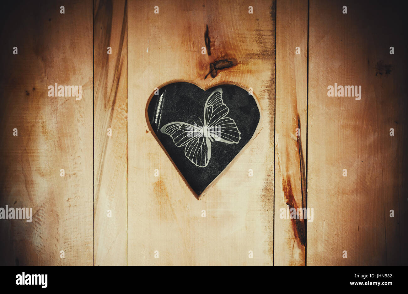 Trou en forme de coeur dans la porte en bois avec des dessins d'un papillon. Banque D'Images