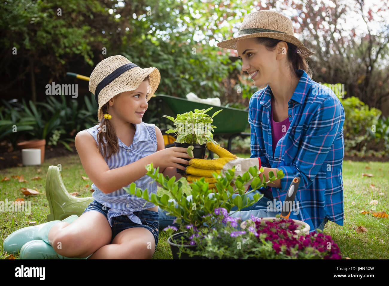 Mère et fille souriante avec des plantes en pots sitting on grass in backyard Banque D'Images