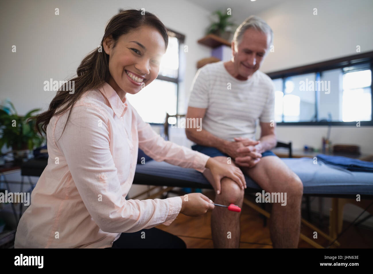 Portrait of female therapist examinant de genou senior male patient avec marteau à réflexe à l'hôpital Banque D'Images