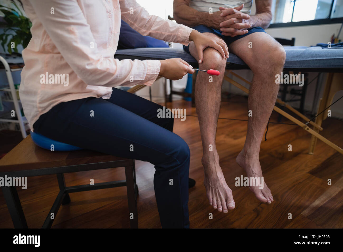 La section basse de female therapist examinant le genou avec marteau à réflexe sur male patient at Hospital ward Banque D'Images