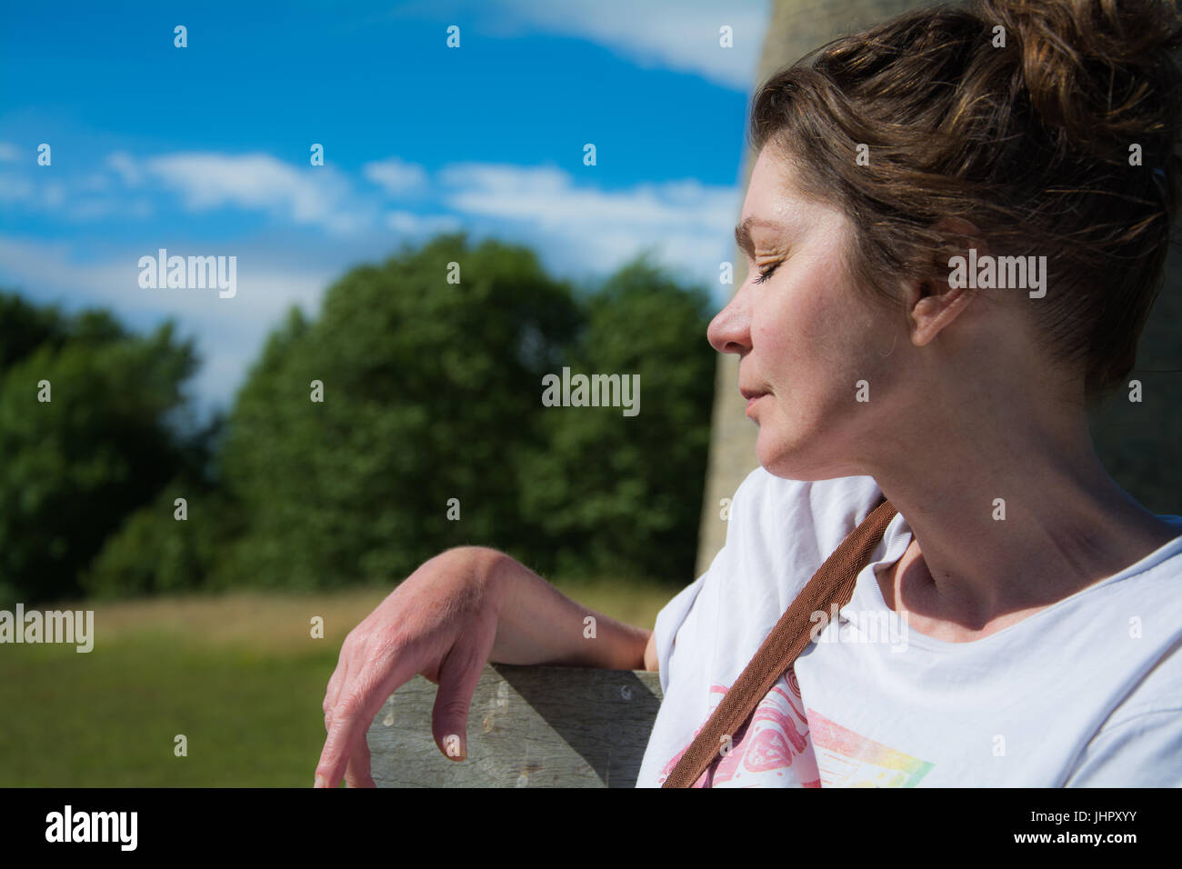 Jolie femme d'âge moyen s'assit en profitant du soleil. L'été, UK. Banque D'Images