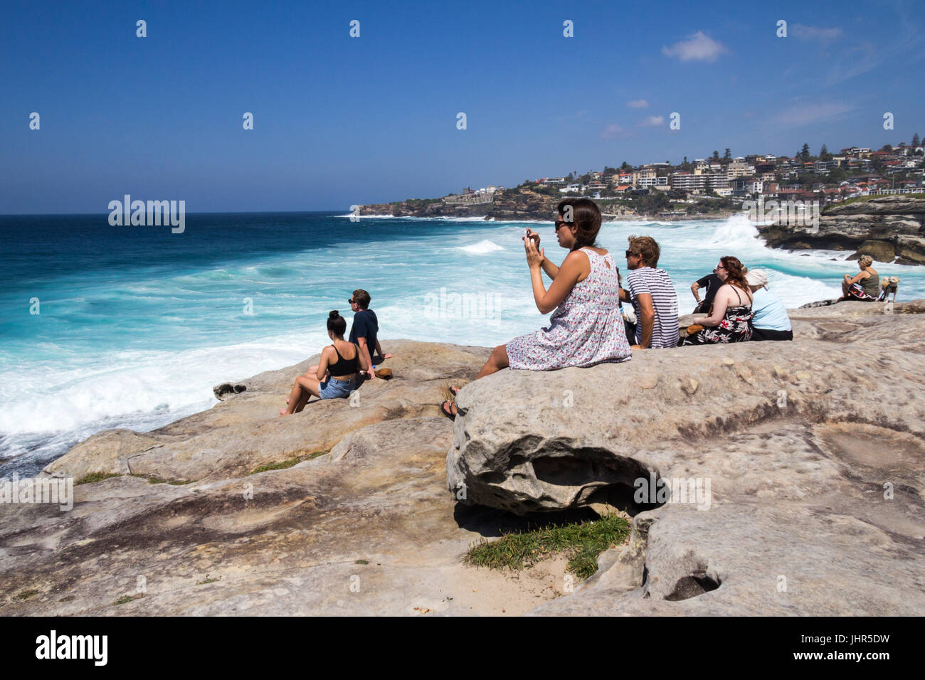Les gens assis en haut d'une falaise à regarder les surfeurs sur la côte de Sydney à Bronte, New South Wales, Australie Banque D'Images