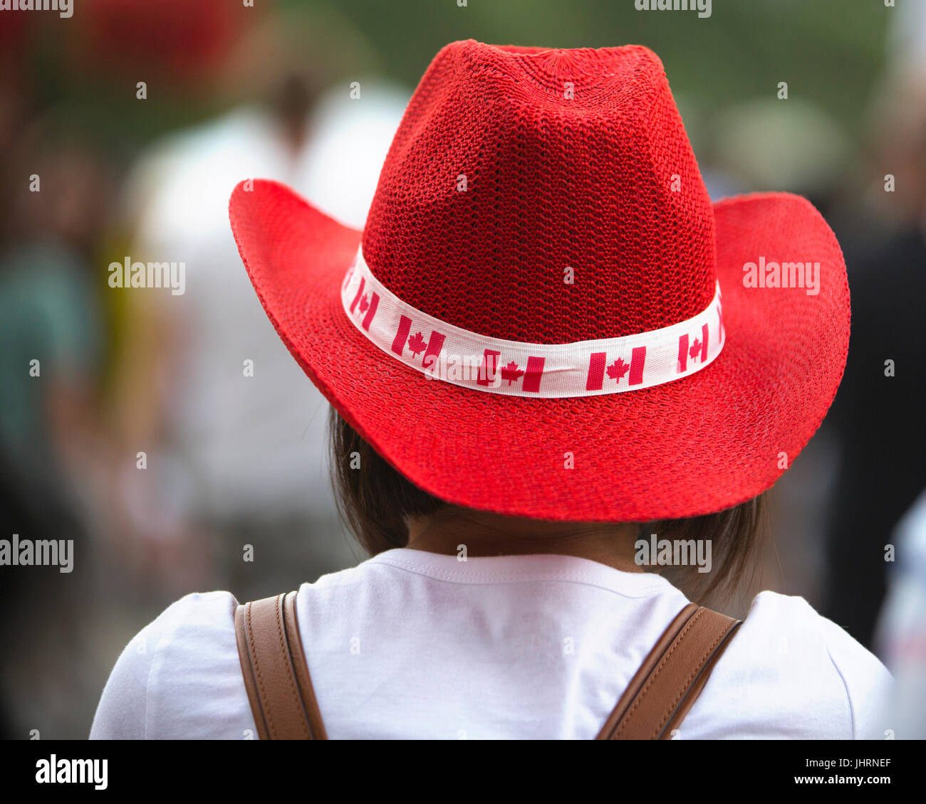 Femme portant chapeau de cow-boy rouge décorée de drapeaux canadiens pour la fête du Canada. La célébration commémore le 150e anniversaire de la confédération. Banque D'Images