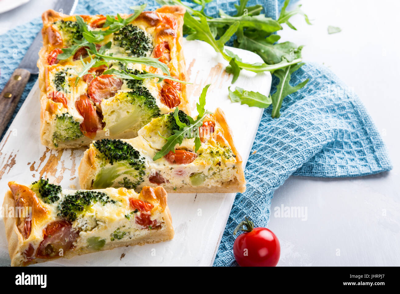 Maison végétariens délicieux gâteau, quiche aux tomates cerise tranchées, de brocoli et de fromage blanc aux herbes sur la vieille planche à découper. Concept d'aliments sains. Banque D'Images