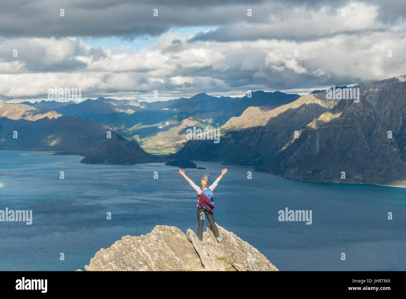 Female hiker sur un rocher, s'étirant les bras en l'air, le lac Hawea et paysage de montagne, Pic isthme, Otago, île du Sud Banque D'Images