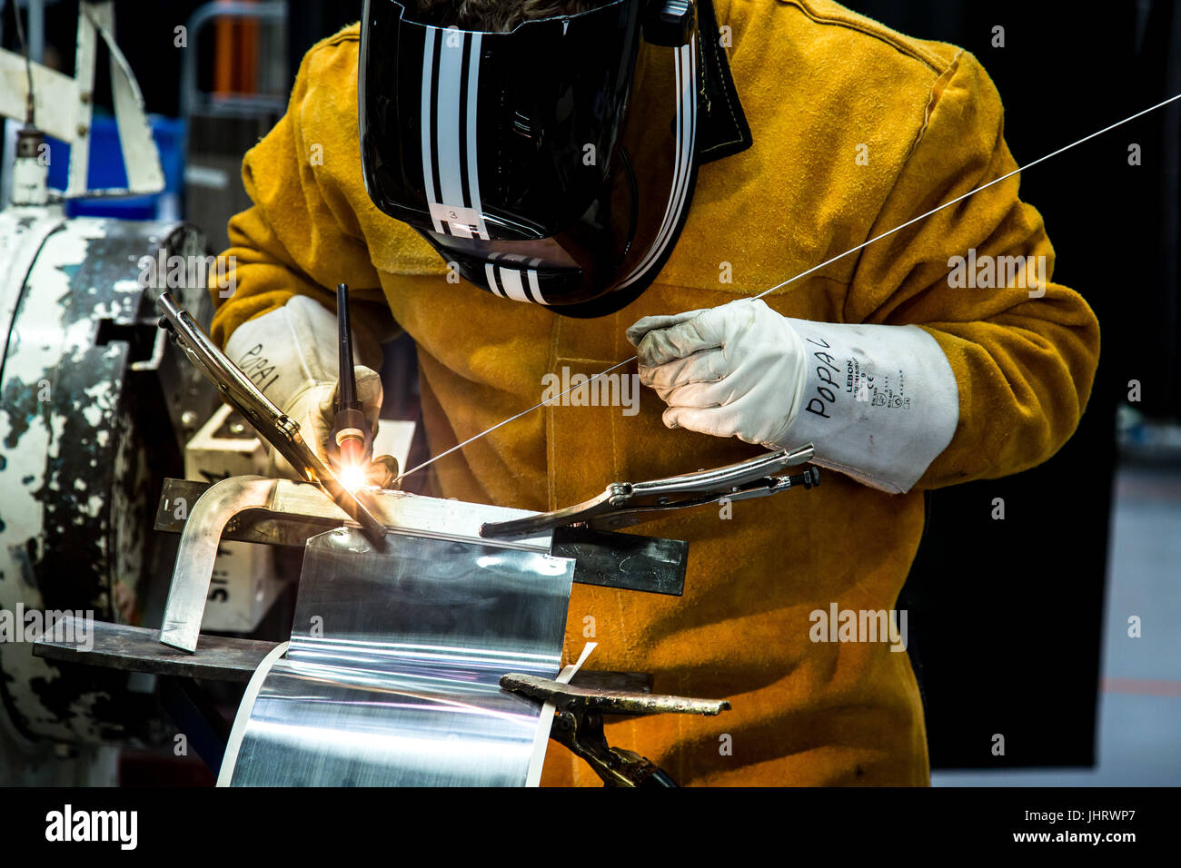 Un soudeur travaillant sur une pièce métallique dans un environnement industriel portant un masque de protection Banque D'Images