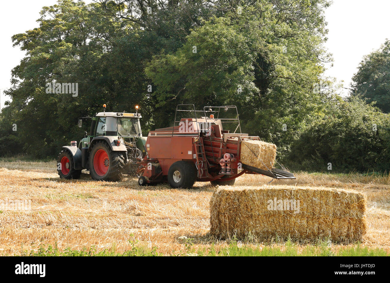 Le tracteur et la mise en balles de foin machine au travail dans un champ Anglais Banque D'Images