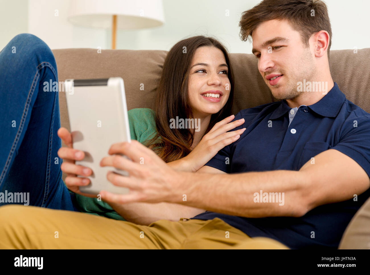 Jeune couple assis sur le canapé et regarder quelque chose sur une tablette Banque D'Images