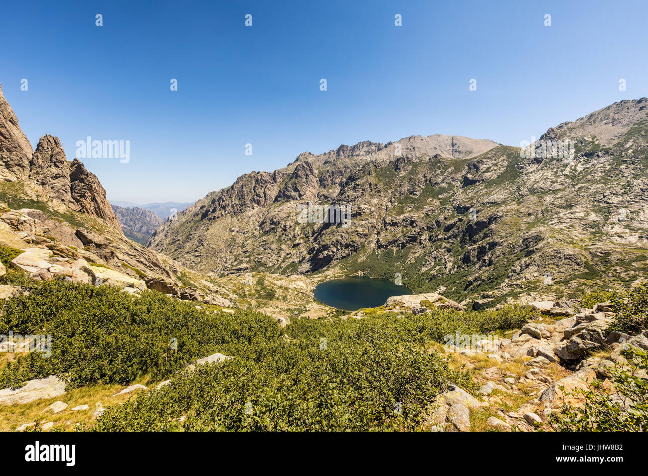 Vue plongeante sur le lac de Melo à la tête de la vallée de la Restonica près de Corte en Corse avec des rochers en premier plan et le ciel bleu Banque D'Images