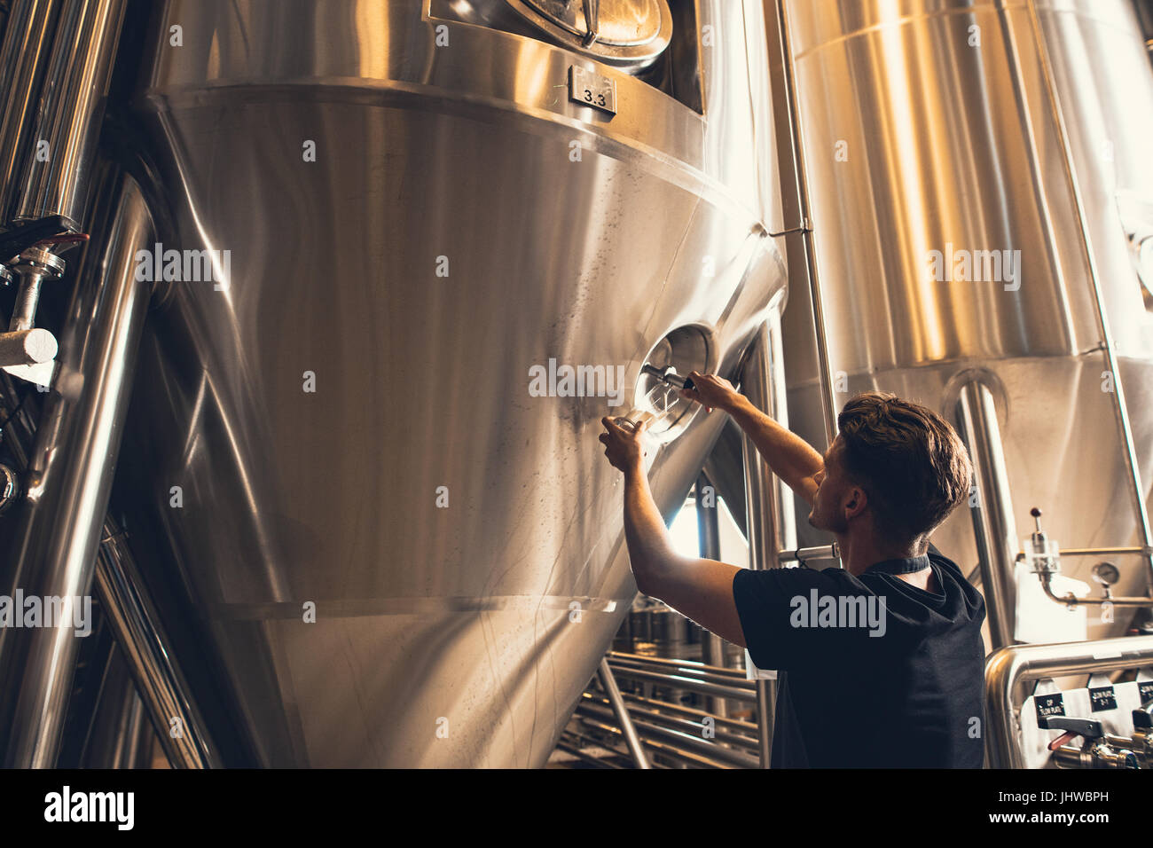 Jeune homme travaillant dans l'usine de fabrication de bière. Brewer travaillant avec l'équipement industriel à la brasserie. Banque D'Images