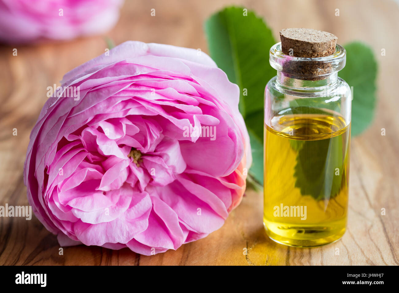 Une bouteille d'huile essentielle avec une fleur rose sur un fond de bois Banque D'Images