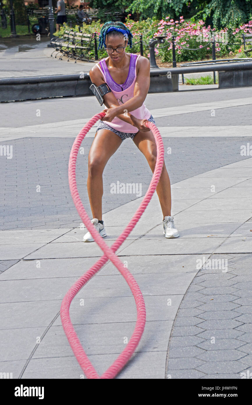 Une jolie jeune femme musculaire fit travailler dehors sur la bataille des cordes pendant un cours de conditionnement physique en plein air à Washington Square Park à Greenwich Village, Banque D'Images