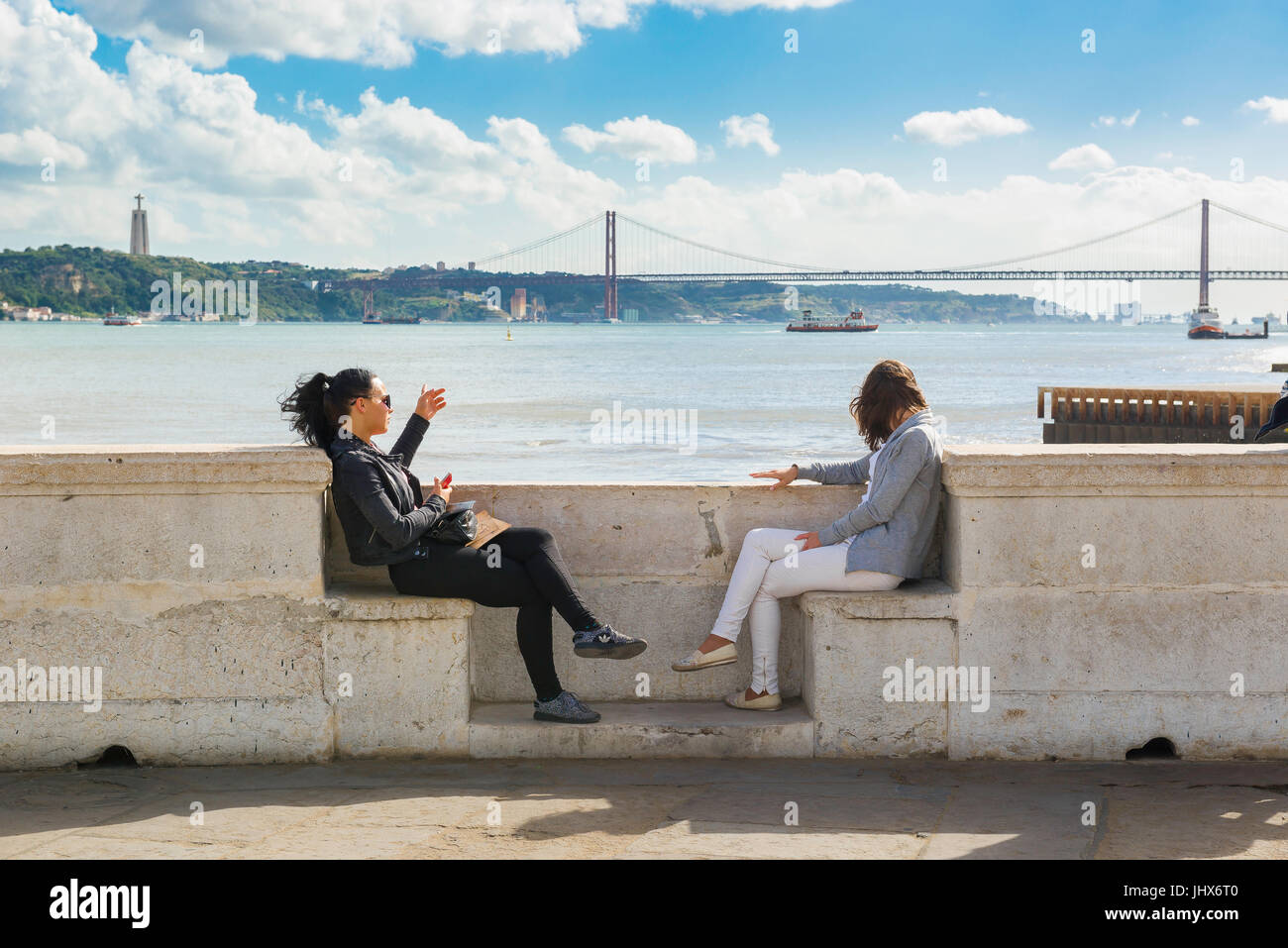 Front de mer de Lisbonne, vue de deux jeunes femmes assis le long de l'Avenida das Ribeira et regardant vers le Tage, Lisbonne, Portugal. Banque D'Images