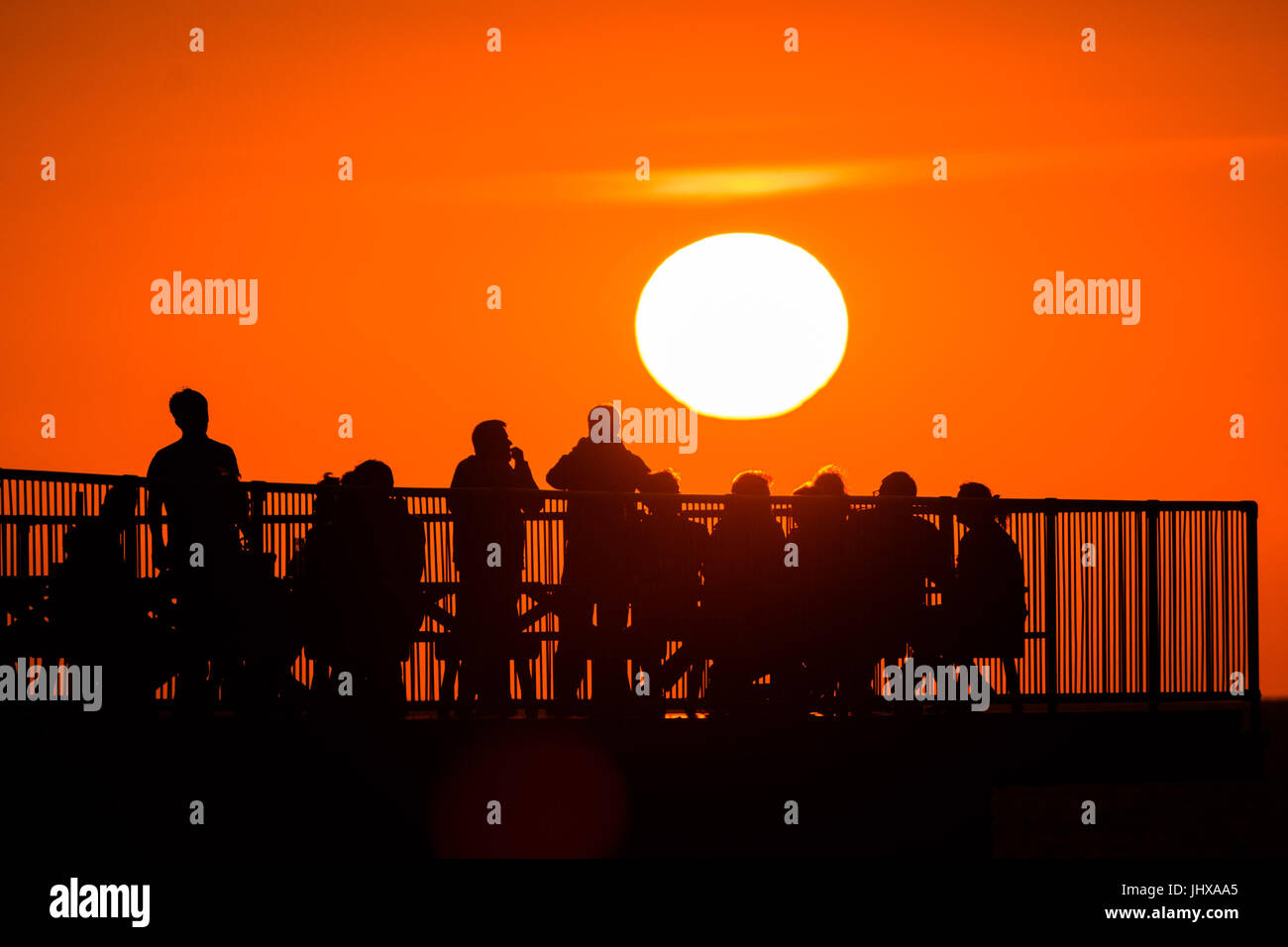 Aberystwyth, Pays de Galles, Royaume-Uni. 16 juillet, 2017. Météo France : des gens assis sur la fin d'Aberystwyth's Victorian station pier, silhouetté au coucher du soleil dans un ciel orange flamboyant sur la baie de Cardigan sur la côte ouest du pays de Galles Crédit photo : Keith Morris/Alamy Live News Banque D'Images