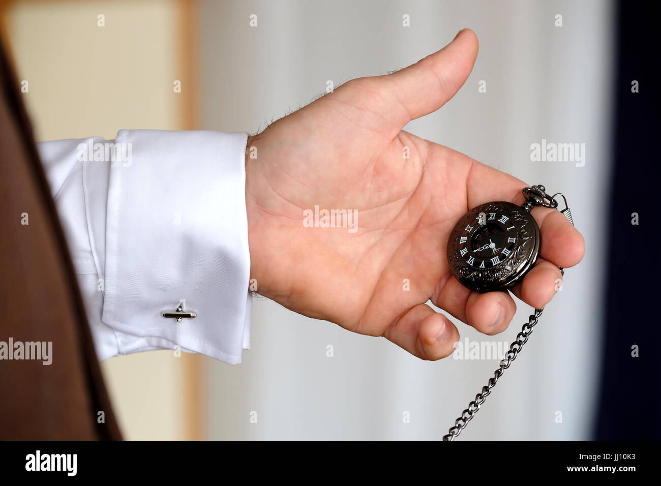 Un homme habillé avec élégance vérifie le temps à l'aide d'une montre de poche attachée à son gilet avec une chaîne. La montre a un visage noir et des chiffres romains blancs Banque D'Images